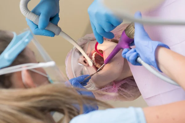 诊所牙医中一名女病人的特写镜头。年轻的金发碧眼的女性张开嘴, 而无法辨认的牙医在乳胶手套检查她的牙齿的条件. — 图库照片