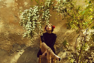 çiçek çiçekler altında hasır sandalye üzerinde oturan kadın