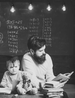 Harika çocuk ve dahi kavramı. Baba, öğretmen okuma kitabı, öğretim çocuk, evlat, kara tahta arka plan. Lisansüstü şapkalı çocuk çocuk dinleme babamı sıkılmış. Baba dahi oğlumu büyümek istiyor.