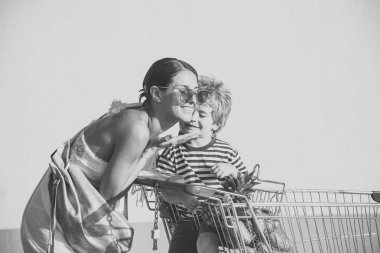 Aile kavramı alışveriş. Mutlu üst sevimli oğlu ile alışverişe. Çocukları ile alışveriş sepeti iterek anne. Anne ve küçük çocuk üzerinde gülümseyen yüzler hugs güneşli, beyaz arka plan.