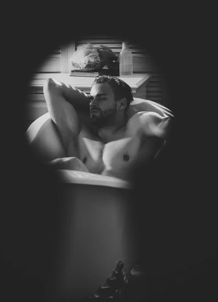 Man relax in bath seen in keyhole, secret