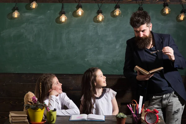 先生の注意を聞いて好奇心旺盛の元気な子ども。背景に黒板の教室で教師と女子生徒。ひげを持つ男は、本を読んで、女子学生を教えています。小学校のコンセプト. — ストック写真