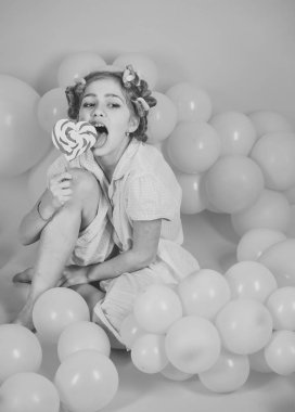 Diyet, doğum günü, punchy pastel, güzellik. Küçük kız çocuk üzerinde pembe lolipop yemek. Çocukluk, mutluluk, tatlı rüyalar. Küçük kız candy lolipop ile. Parti balonları, çocukta curlers, pijama moda