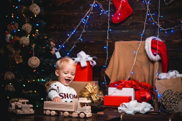 Szczęśliwy, że małe dzieci w santa hat z obecnie mają Bożego Narodzenia. Słodkie małe dziecko jest dekorowanie choinki pomieszczeniu. Zimowy wieczór w domu. Radosne dziecko patrząc na kamery w Boże Narodzenie w domu. — Zdjęcie stockowe