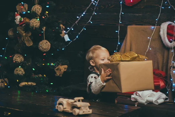 Winterkinder. Kinder genießen den Urlaub. Weihnachtskarte. Neujahrskinder. glückliches Kind mit Weihnachtsgeschenkbox. Frohe Weihnachten und frohe Feiertage. Lächelndes Kind lugt hinter Baum im Wohnzimmer hervor. — Stockfoto