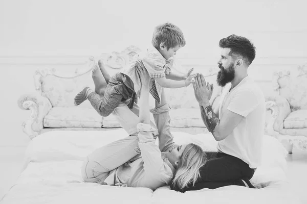 母亲和父亲抱着可爱的儿子。年轻的家庭在床上共度时光, 奢华的室内背景。父母带着快乐的面孔关注孩子, 玩耍, 玩得开心。幸福家庭理念. — 图库照片