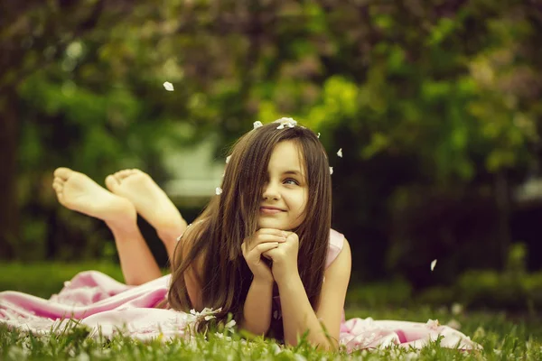 Meisje op groene gras met bloemblaadjes — Stockfoto