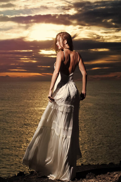 Pretty girl in white dress stands at dark sea shore