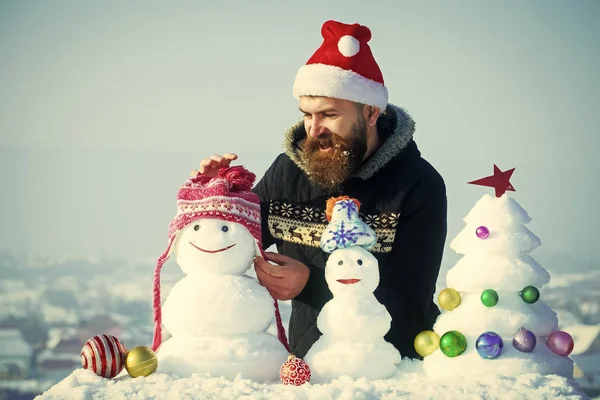 Feliz hombre de Santa poner sombrero en muñeco de nieve — Foto de Stock