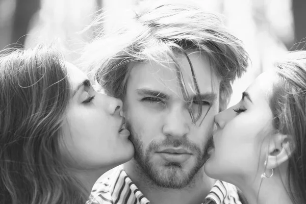 Two pretty girls kissing unshaven man