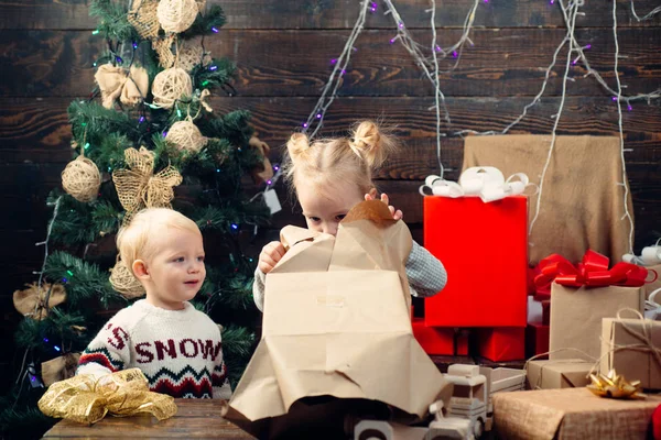 Porträt Kind mit Geschenk auf Holzgrund. Niedliches kleines Kind schmückt den Weihnachtsbaum drinnen. fröhliches kleines Kind in Winterkleidung denkt an Weihnachtsmann in der Nähe des Weihnachtsbaums. — Stockfoto