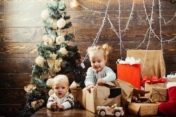 Süße kleine Kinder, die Weihnachten feiern. christmas kids - Glückskonzept. Kindergeschenk. niedliches kleines Kind in der Nähe des Weihnachtsbaums. glückliches Kind mit einem Weihnachtsgeschenk auf Holzgrund. — Stockfoto