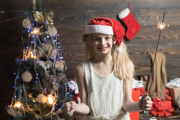 Lycklig liten flicka klädd i vinter kläder tycker om Santa nära julgran. Barn njuta av semestern. Vinterkväll hemma. God Jul. Tonåringen nyår. — Stockfoto