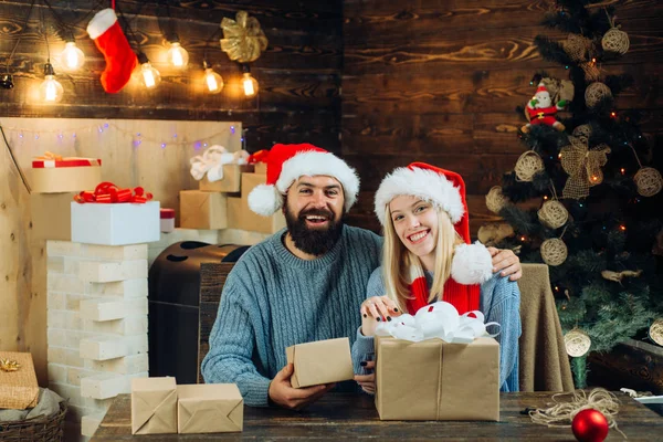 Porträtt av en ung vacker leende par. Vinter semester och människor koncept. Vackra par klädd i en jultomten hatt. Julgran dekorera hemma. — Stockfoto