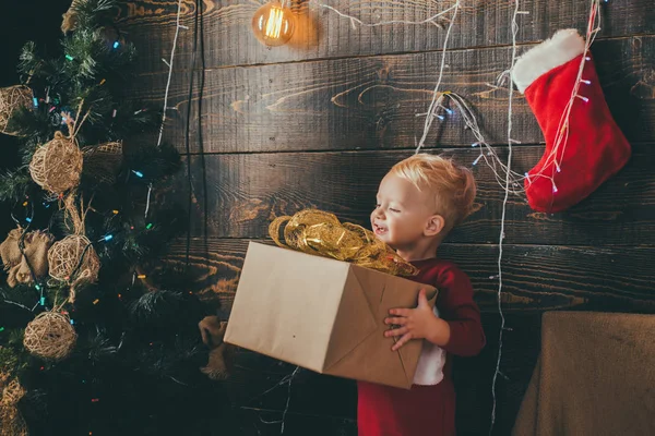Kind mit Weihnachtsgeschenk auf hölzernem Hintergrund. Weihnachtskarte. süße kleine Kinder, die Weihnachten feiern. glückliches Kind mit Weihnachtsgeschenkschachtel. — Stockfoto
