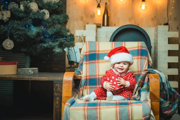 Niedliches kleines Baby schmückt den Weihnachtsbaum drinnen. Weihnachten Winterurlaub Konzept. glückliches Kind mit Weihnachtsgeschenk. — Stockfoto