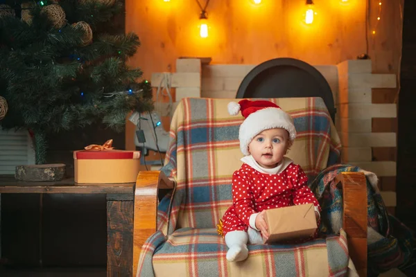 Glückliches Kind mit Weihnachtsgeschenk. niedliches kleines Baby schmückt den Weihnachtsbaum drinnen. Weihnachtsferien-Konzept. — Stockfoto