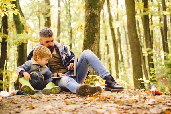Батько навчає дитину. Тато і син використовують ноутбук у парку. Батько і син грають в осінньому лісі . — стокове фото