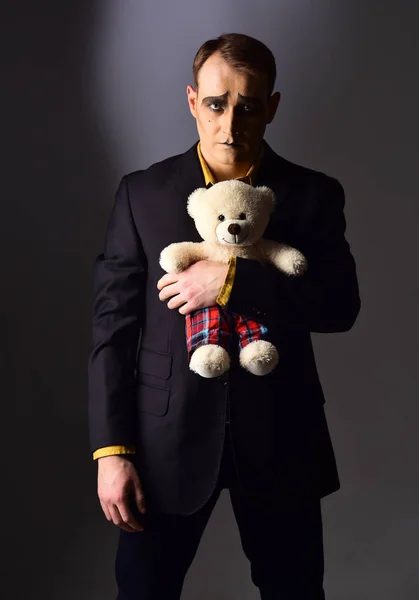 Depressed and lonely. Mime man hold teddy bear toy. Stage actor with mime makeup in toy shop. Theatre actor miming sad emotions. Unhappy mime artist. Theatrical performance art and pantomime drama