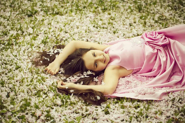 Little girl on green grass with petals — Stock Photo, Image