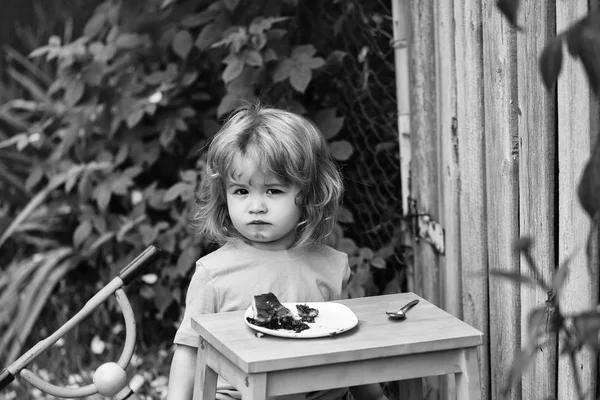 Mały chłopiec jedzenie tortu w pobliżu ogrodzenia drewniane — Zdjęcie stockowe