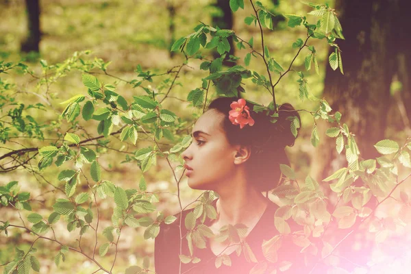 Jolie fille avec fleur dans les cheveux posant dans les feuilles vertes — Photo