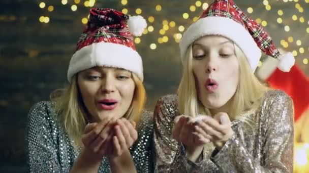 Le ragazze in cappelli Di Capodanno che soffiano la neve da mani. Che soffia neve dalle mani. Concetto di umore di anno nuovo. Inverno incantevole . — Video Stock