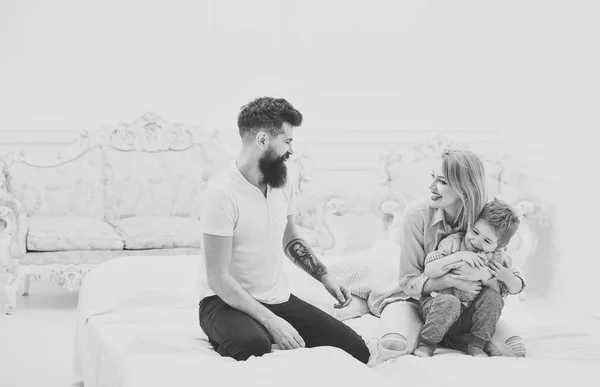 Jovem família passar tempo juntos na cama, fundo interior de luxo. Mãe e pai abraçando com o filho bonito. Os pais com rostos felizes prestam atenção à criança, brincam, divertem-se. Conceito de família feliz — Fotografia de Stock