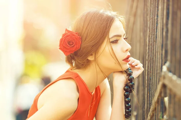 Nachdenkliches Mädchen mit roten Rosen im Haar und schwarzen Perlen — Stockfoto