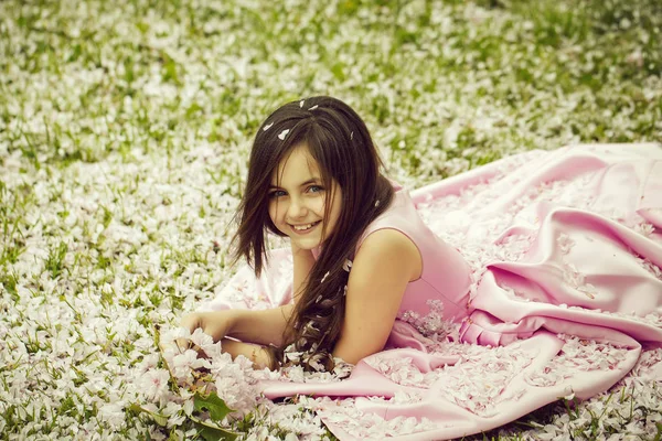 Little girl on green grass with petals — Stock Photo, Image