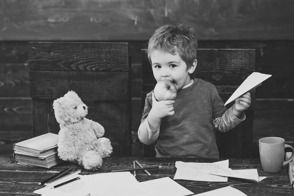 Il ragazzo mangia una mela succosa. Un ragazzo biondo con un aereo di carta in mano. Adorabile bambino nella scuola materna — Foto Stock