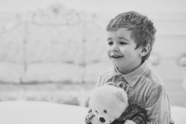 Мальчик со счастливым лицом держит любимого игрушечного пушистого медведя. Детские игры с плюшевым медведем, роскошный внутренний фон. Ребенок с мягким плюшевым мишкой в руках. Счастливое детство. Маленький милый малыш носит игрушку — стоковое фото