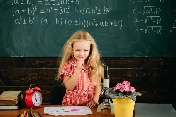 Маленькая девочка стоит на фоне доски. Девушка в классе. Счастливый дошкольник — стоковое фото