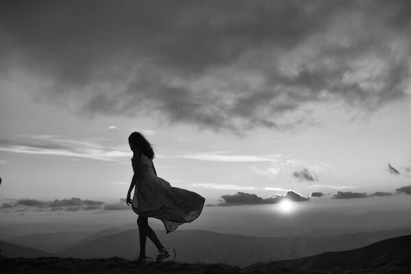 Woman or girl silhouette walking at beautiful view on sunset or sunrise in blue sky with clouds and yellow orange sun in mountains on natural background.