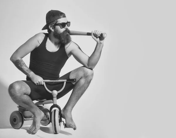 Bearded angry man holds green baseball bat on bicycle toy — Stock Photo, Image