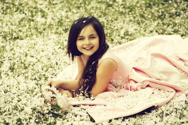 Little girl on green grass with petals — Stock Photo, Image