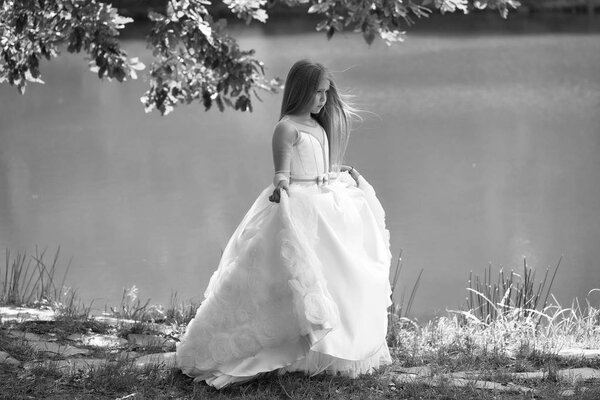 Small girl kid with long blonde hair and pretty smiling happy face in prom princess white dress standing sunny day outdoor near water