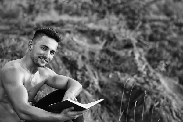 Homme musclé souriant avec livre en plein air — Photo