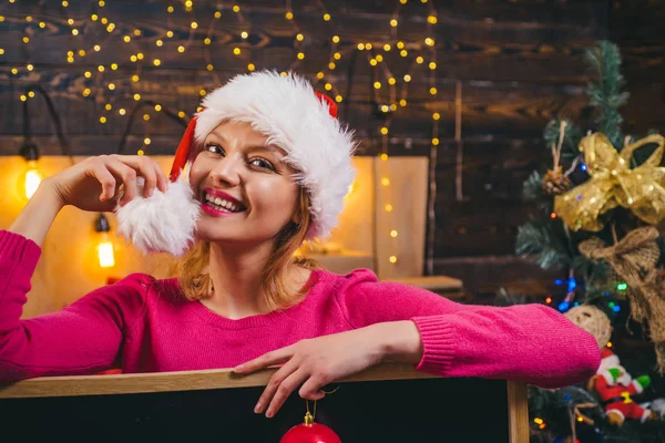 Mujer con sombrero rojo de Santa sosteniendo presente. Mujer rubia Santa sosteniendo caja de regalo en la pared vintage. Moda navideña. Chica de lujo celebrando Año Nuevo. Mujer Navidad . — Foto de Stock