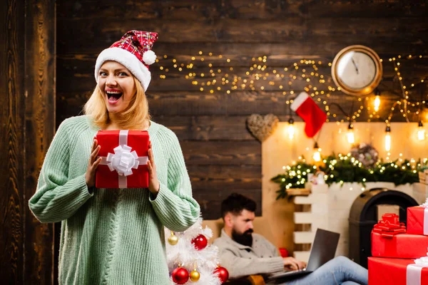 Vi önskar dig en god jul. Par i kärlek med nuvarande julklapp framför julgranen. Hipster vänner ny åren aftonen. — Stockfoto