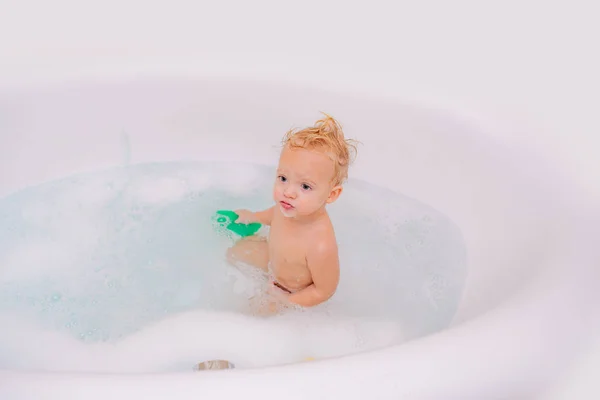 Adorable niño rubio divirtiéndose con agua tomando un baño en la bañera. Baño divertido para niños . —  Fotos de Stock