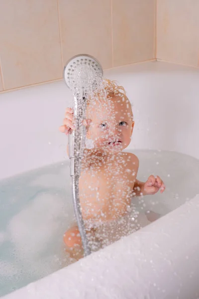 Söt glad skrattande baby i mjuk badrock efter bad leker i barnkammaren. Trevlig liten unge spelar i badkar. Baby bad leksaker. — Stockfoto