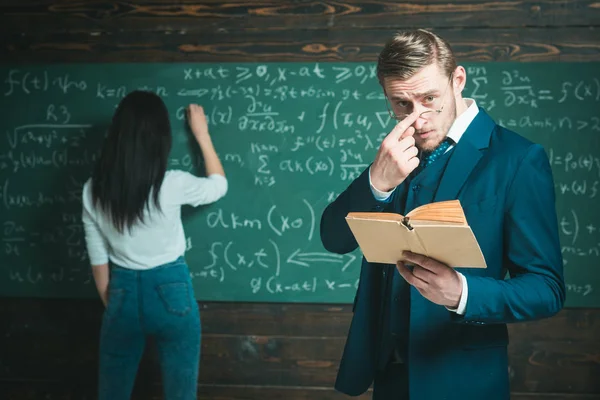 Leren math stelt mij in staat om helder te denken. Leraar man in glazen gelezen probleemstelling uit leerboek voor meisje student. Achterzijde weergave vrouw vergelijking op schoolbord schrijven. Doen bedragen. Schooldag — Stockfoto