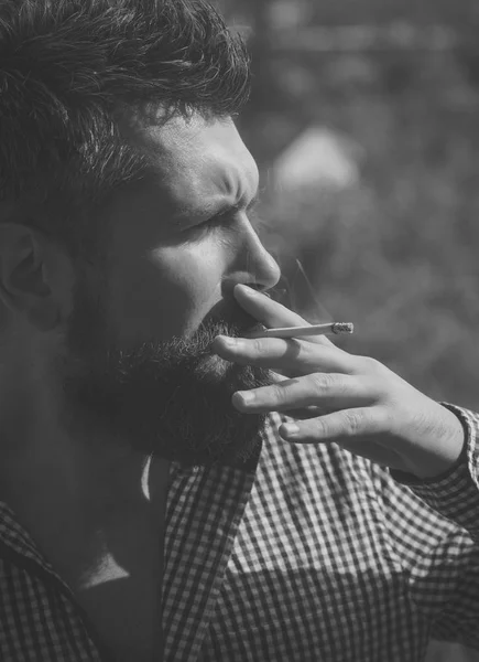 Hombre fumando cigarrillo. joven barbudo hipster con barba y bigote en la cara seria fumar cigarrillos al aire libre. estilo de vida poco saludable y mal hábito de chico con adicción. peluquería y peluquería —  Fotos de Stock