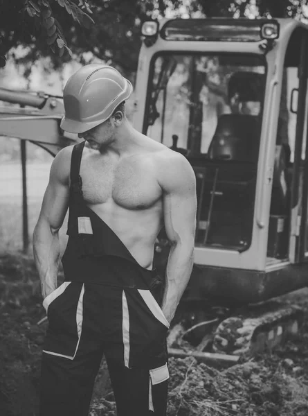 Muscular builder in hard hat wears overalls. — Stock Photo, Image
