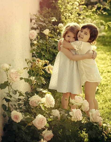 As crianças que sorriem em flores de rosa florescentes — Fotografia de Stock