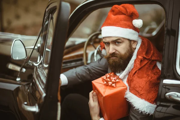 冬季假期庆典 有严重的脸的圣诞老人保持当前框 圣诞节和新年的季节 时髦的红帽提供圣诞礼物在复古汽车 拳击日概念 — 图库照片