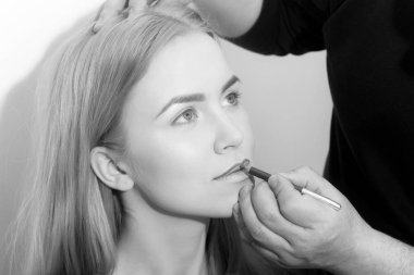 Kırmızı kalem kadın dudaklarından uygulama visagiste el. Genç yüz, sağlıklı cilt makyaj temeline ve gri arka plan üzerinde sarı uzun saçları olan kız. Sima, kozmetik, Cilt Bakımı, makyaj. Güzellik Salonu