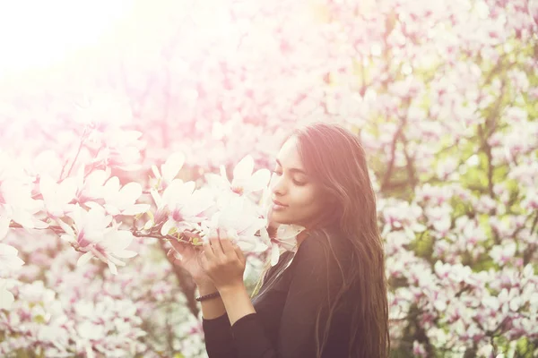 可爱的女孩或漂亮女人与黑发 长长的头发享受着粉红色 玉兰鲜花盛开 在阳光明媚的日子 对模糊的花艺环境开花公园的树上 做白日梦 繁荣和春天 — 图库照片