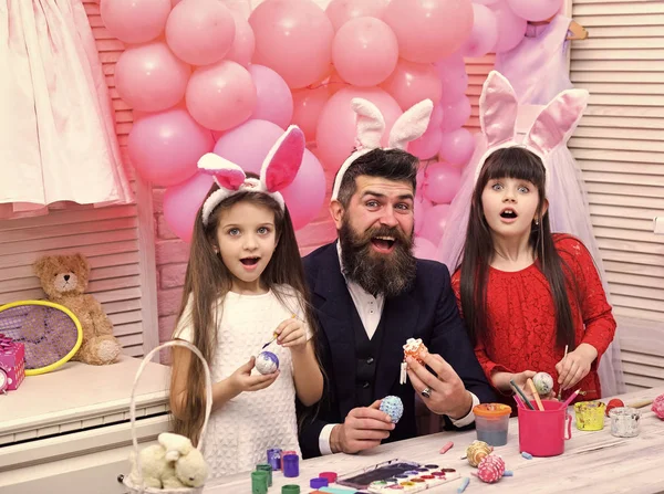 Happy easter family paint eggs. Father and daughters paint handmade egg. Easter, father and children in pink bunny ears. Family values, childhood, art. Happy family celebrate spring holiday, love.